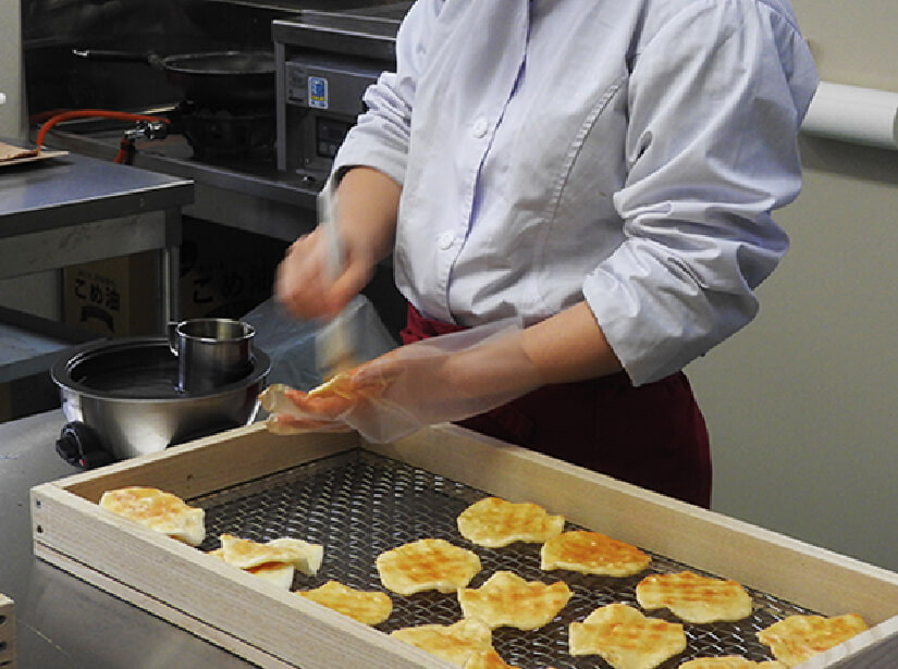 焼き上がったせんべいを、１枚１枚ていねいに味付けをして完成です